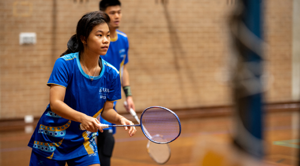 A UWA Student prepares to serve in Badminton while wearing the UWA representative uniform