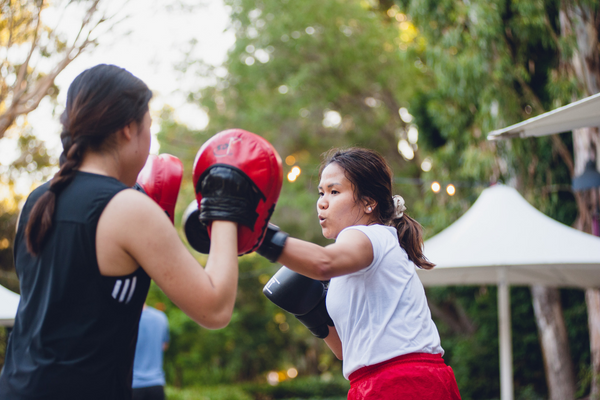 Two women, one wearing boxing pads and the other boxing gloves, participating in a boxing for fitness class.