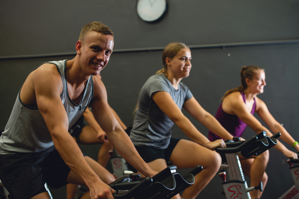 A man and a woman, both UWA students, ride on stationary bikes at the UWA Gym.