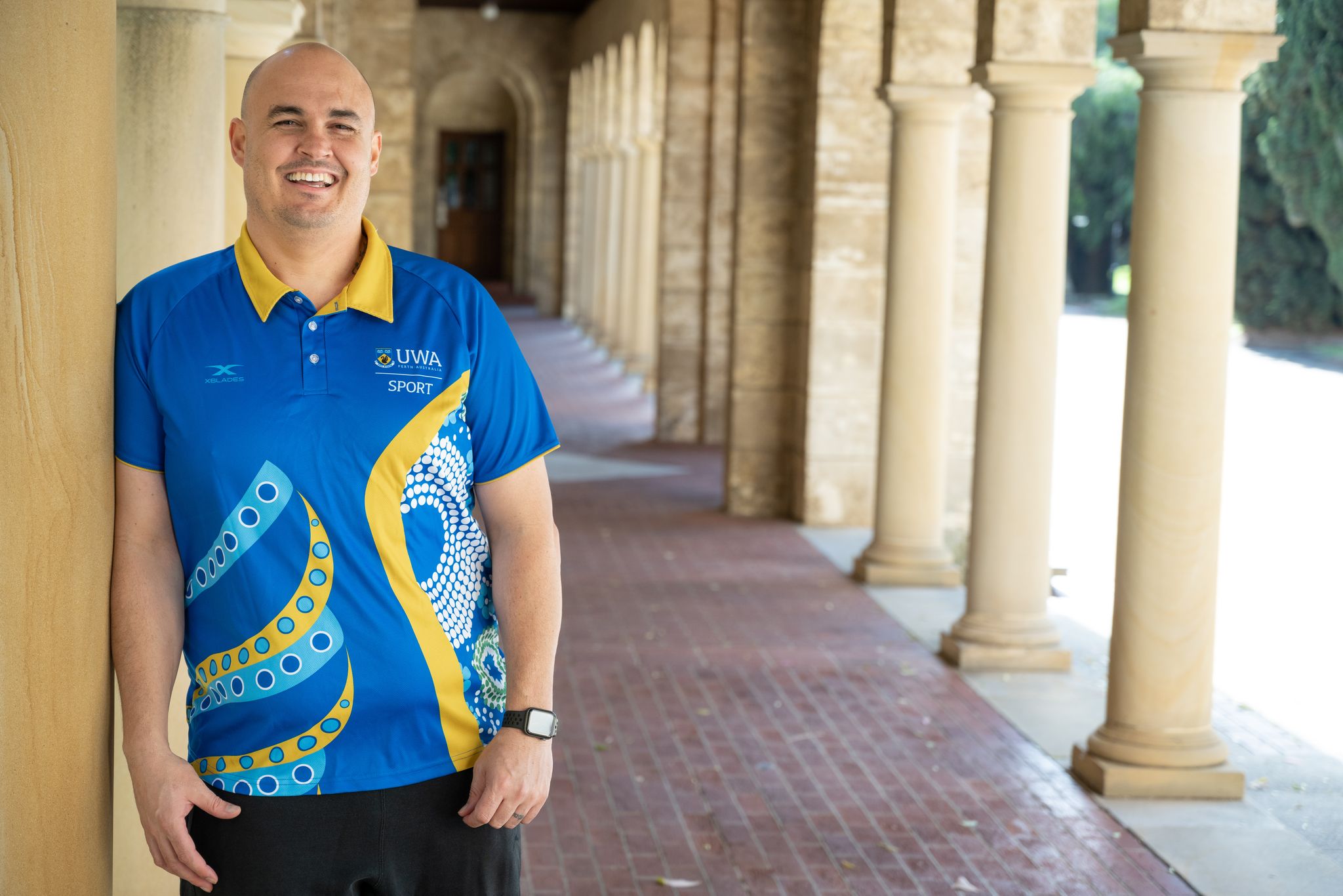 Aaron Sutton stands in front of a sandstone pillar at UWA, wearing the Maali strip he designed.
