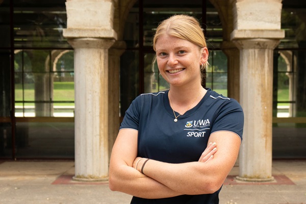 Mia Mather standing, arms folded, in front of sandstone structures at UWA