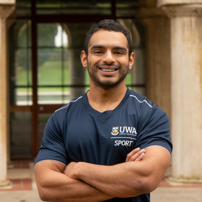 Micky Sivakumar stands in front of the sandstone pillars of Winthrop Hall with his arms crossed, smiling into the camera. 