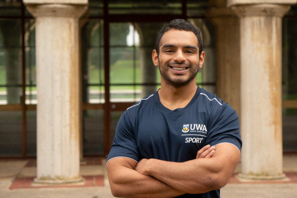 Micky Sivakumar stands in front of the sandstone pillars of Winthrop Hall with his arms crossed, smiling into the camera. 