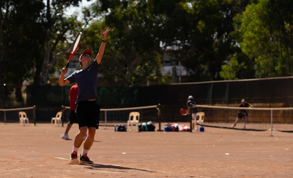 A UWA Tennis Club member serves a ball on a red clay court