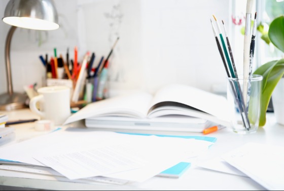 Open book on a desk with pot plants, notes and stationery surrounding it