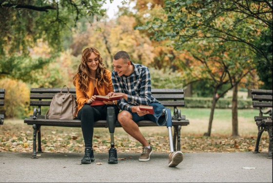 Two people with one prosthetic leg sitting on a park bench