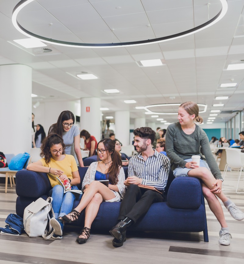 A group of students sitting in a library talking to each other. 