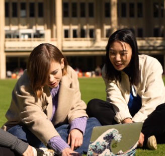 Two students sitting on grass looking at laptop
