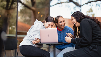 Three female indigenous students sitting at a table using a laptop