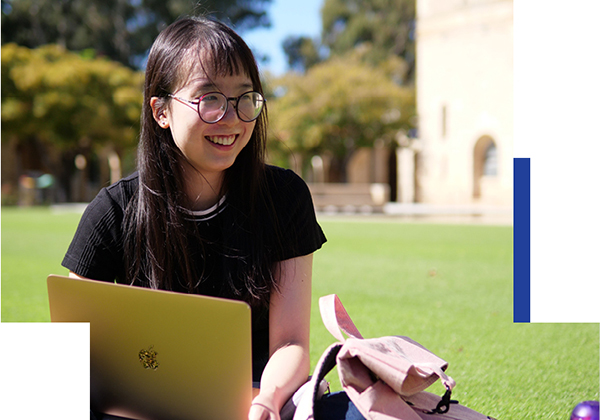 Student with laptop sitton on grassed area at UWA