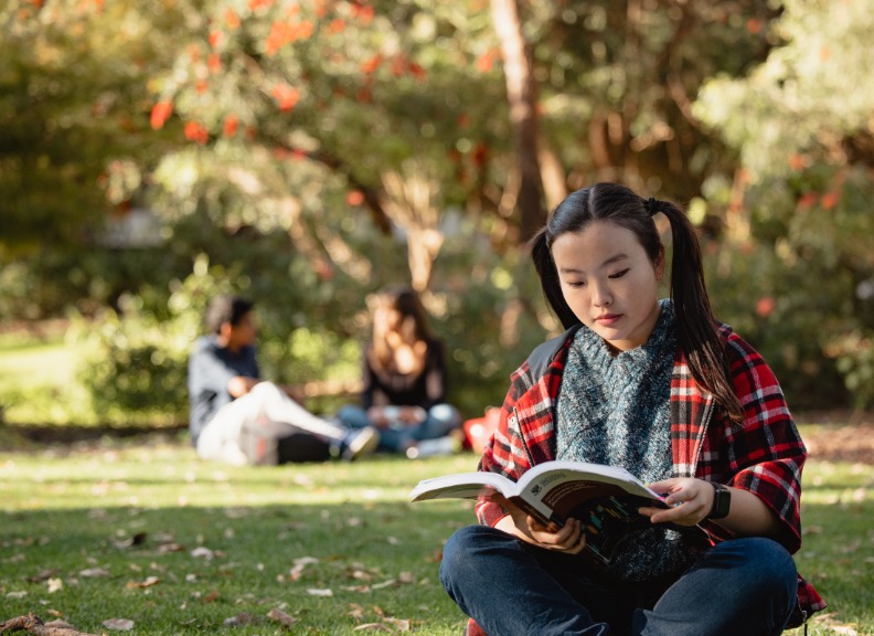 Student sitting on grass reading book