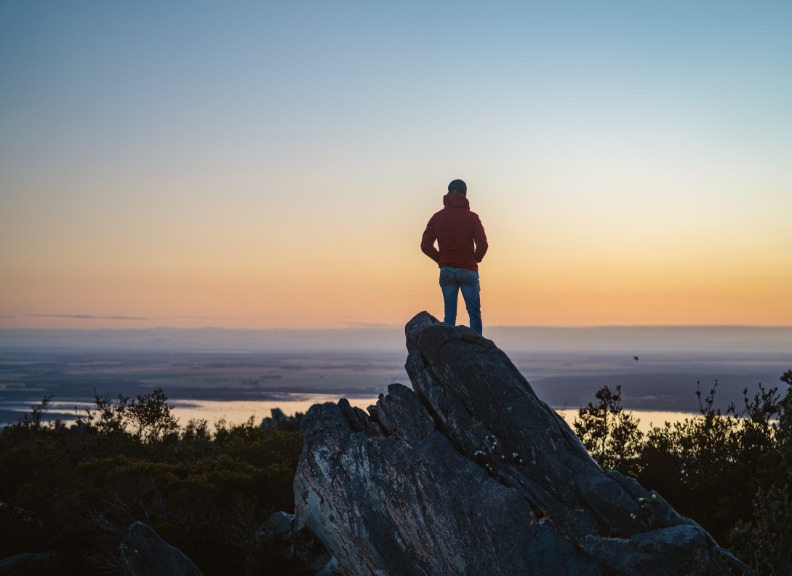 Lone man standing on the top of East Mount Barren as the sun rises behind him. Located in the Fitzgerald River National Park in Hopetoun, Western Australia