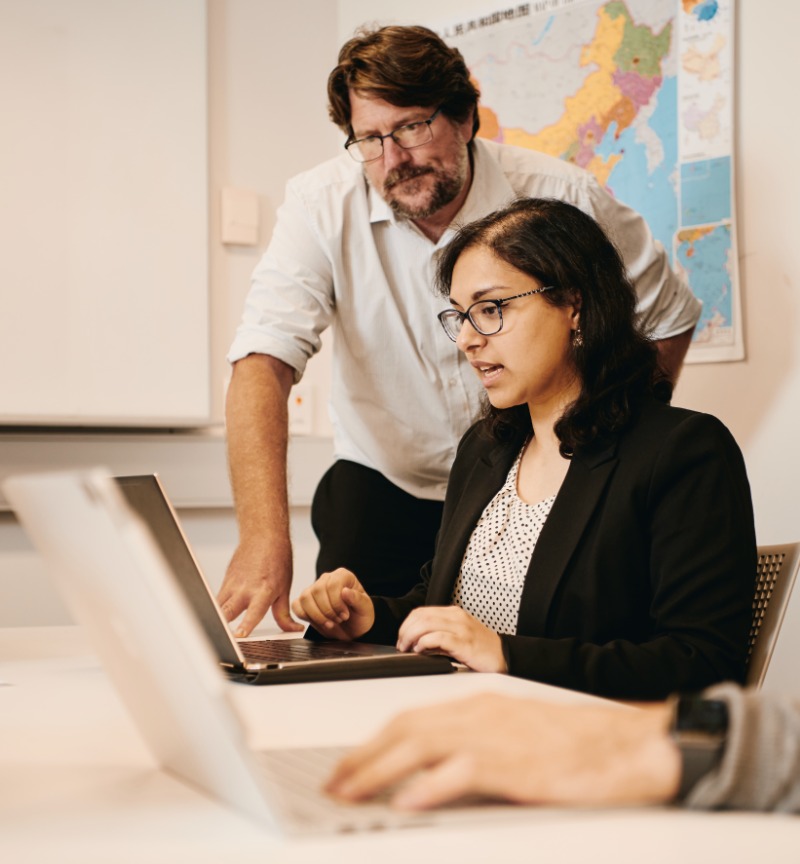 Teacher standing next to a student looking at a laptop