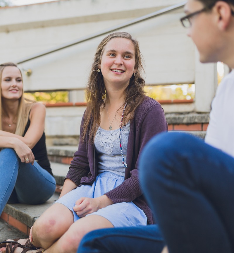 3 people sitting on a set of stairs chatting. 