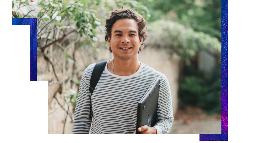 UWA student carrying laptop and backpack stands outside in front of a wall with greenery smiling at the camera wearing a white and black horizontally striped tshirt