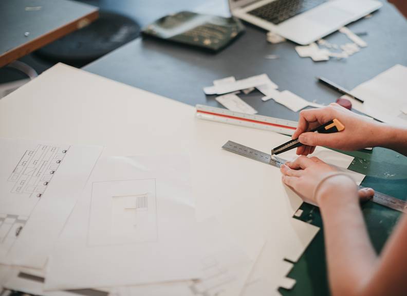 Person working on architectural drawings and scale models with rulers and paper on a design workspace